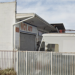 A polícia de San Diego apreende 62 caça-níqueis, drogas e dinheiro em apreensões de jogos ilegais. Exterior de uma pequena oficina de automóveis com portão de segurança de metal e uma placa dizendo “MGK Auto”, com um caminhão branco estacionado na frente, ilustrando o local conectado a uma apreensão de jogos ilegais da polícia de San Diego, onde máquinas caça-níqueis, drogas e dinheiro foram apreendidos.