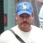 Ryan Wedding, homem de bigode e chapéu azul, procurado por tráfico de drogas, em foto de vigilância.