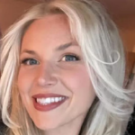 Uma mulher com óculos escuros e longos cabelos loiros olha para a câmera. Ela está com um vestido laranja queimado e segura uma taça de vinho branco. É um tiro na cabeça e nos ombros.