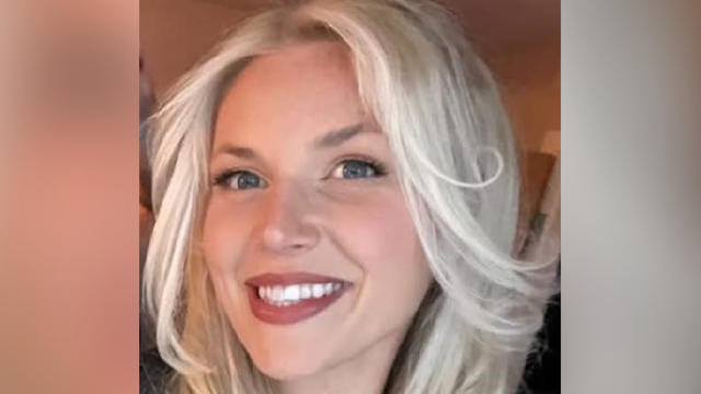 Uma mulher com óculos escuros e longos cabelos loiros olha para a câmera. Ela está com um vestido laranja queimado e segura uma taça de vinho branco. É um tiro na cabeça e nos ombros.