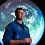 Um homem e uma mulher em um palco com a apresentação de uma viagem à lua atrás deles.