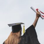 Rear view of woman in a cap and gown holding a diploma in the air.
