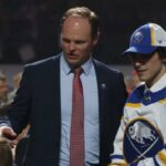 O gerente geral Kevyn Adams do Buffalo Sabres (L) apresenta Matthew Savoie ao pessoal da equipe em sua mesa de recrutamento