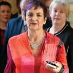 Douglas Ross, de terno escuro, camisa azul e gravata cor de vinho, está de pé no parlamento. Ele está gesticulando com as duas mãos, claramente defendendo um ponto de vista em um debate.