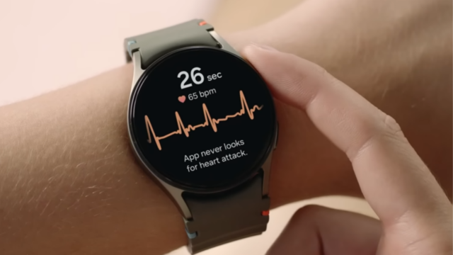 Samsung Galaxy Watch 7 em um suporte, mostrando a tela inicial com outros produtos Galaxy em segundo plano