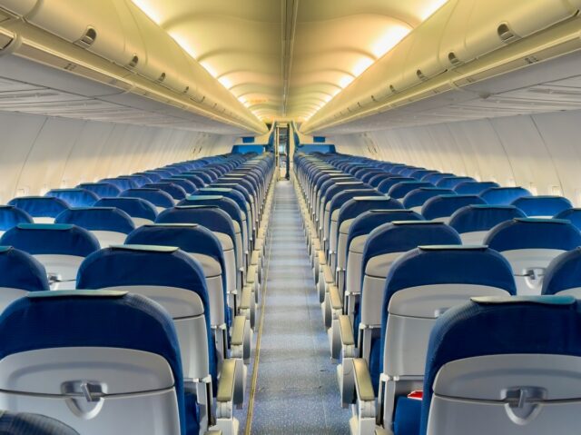 A stock image showing an aisle view of an empty commercial aircraft.