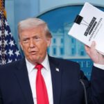 Donald Trump displays a stack of papers labeled