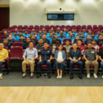 Os embaixadores da Polícia de Singapura sentaram-se numa pequena sala semelhante a um auditório. A Polícia de Cingapura anuncia novos embaixadores de trabalhadores migrantes, trabalhando para lidar com os riscos do jogo