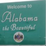 Placa verde na beira da estrada onde se lê “Bem-vindo ao Alabama, o Belo”, com o selo do estado abaixo do texto. A ação coletiva do Alabama visa derrubar a iniciativa de apostas esportivas de Kalshi