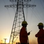 Two workers inspect high-tension power lines.