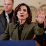 Kathy Hochul falando em um pódio com a mão levantada.