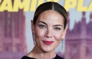 A máscara de luz vermelha para redução de rugas de Michelle Monaghan tem 30% de desconto Uma mulher madura usa sua máscara facial de LED vermelho (terapia de luz vermelha) enquanto relaxa em casa, em uma poltrona. Ela usa seu smartphone - Fotografia de stock