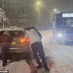 Pessoas tentam empurrar um carro preso na neve em Buxton, Peak District, Derbyshire, na noite de quinta-feira