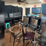 A polícia de San Diego invade uma operação de jogo ilegal em uma casa em City Heights. Uma pequena sala com várias máquinas de jogo estilo caça-níqueis alinhadas em mesas, cadeiras espalhadas e cortinas pretas cobrindo as janelas.