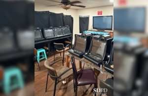 A polícia de San Diego invade uma operação de jogo ilegal em uma casa em City Heights A polícia de San Diego invade uma operação de jogo ilegal em uma casa em City Heights. Uma pequena sala com várias máquinas de jogo estilo caça-níqueis alinhadas em mesas, cadeiras espalhadas e cortinas pretas cobrindo as janelas.