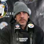 Um homem vestindo um gorro cinza e um moletom escuro, falando em dois microfones com os logotipos da NFL e dos Steelers.