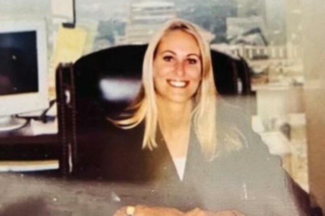 Rachel Green sorrindo enquanto está sentada em uma mesa.