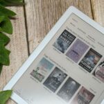 Uma mulher sentada em uma cadeira lendo um livro, com ícones coloridos do NotebookLM flutuando ao seu redor e uma pilha de livros no chão ao lado da cadeira