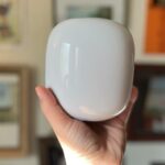 Segurando o Google Nest Wifi Pro com fotos e arte em segundo plano