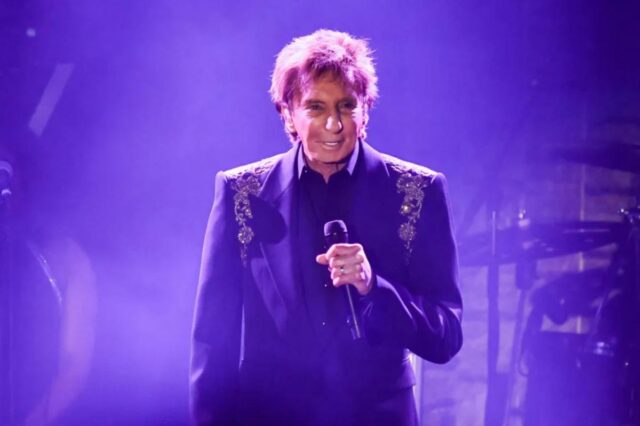 Barry Manilow se apresentando no palco com um microfone.