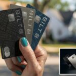 Uma mão segurando três cartões de crédito Bilt em preto, prata e azul, contra um fundo suburbano desfocado.