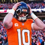 O quarterback do Denver Broncos, Bo Nix, vestindo uma camisa laranja com o número 10, colocando seu capacete com