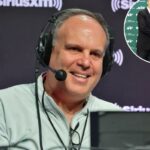 Um homem usando um fone de ouvido e uma jaqueta de cor clara sorri diante de um fundo com o logotipo SiriusXM.