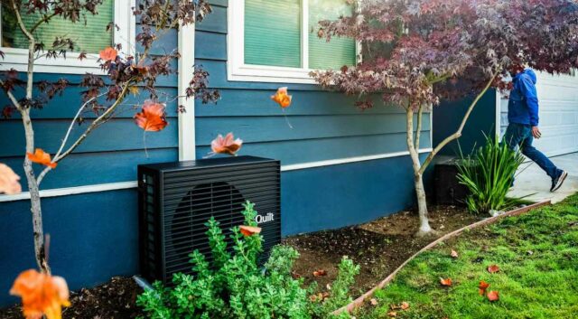 Como a Quilt resolveu o maior desafio da bomba de A dark grey heat pump sits outside a blue home.