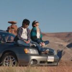 Jenny Slate e Chris Pine caminhando juntos do lado de fora de uma lanchonete em