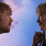 Jenny Slate e Chris Pine caminhando juntos do lado de fora de uma lanchonete em