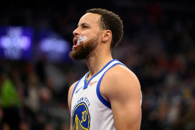 O guarda do Golden State Warriors, Stephen Curry, centro, tem a bola desviada pelo atacante do Utah Jazz, Kyle Filipowski, à direita, enquanto ele dirigia para a cesta durante o primeiro tempo de um jogo de basquete da NBA, quarta-feira, 28 de janeiro de 2026, em Salt Lake City. (Foto AP/Tyler Tate)