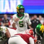 O quarterback do Oregon Ducks, Dante Moore (5), convoca uma jogada na linha de scrimmage contra o Indiana Hoosiers durante o primeiro quarto do Peach Bowl de 2025 e o jogo semifinal do College Football Playoff no Mercedes-Benz Stadium.
