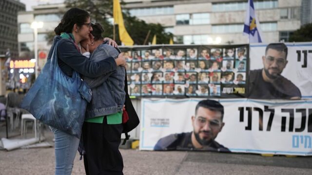 Duas mulheres abraçam-se junto a uma faixa com uma fotografia de Ran Gvili após o anúncio de que o refém, cujos restos mortais foram os últimos a serem recuperados em Gaza, tinha sido identificado.