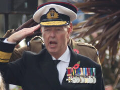 Espada suspeita e medalha rara – como o falso almirante foi finalmente descoberto Um homem vestido de almirante faz uma saudação. Ele usa chapéu branco, jaqueta azul marinho, camisa branca e gravata. No peito há uma série de medalhas penduradas por fitas coloridas.