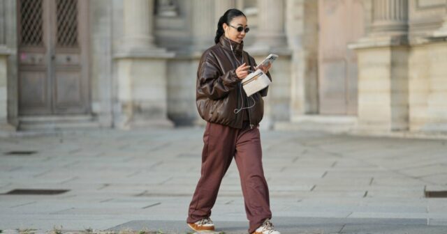 Patricia Wirschke é vista vestindo um clássico casaco longo Herno bege, com gola entalhada, aba de proteção e punhos com cinto; um conjunto Incentive cor bordô com um suéter tricotado, com bainha, punhos e decote canelados e calças tricotadas de perna larga com corte descontraído; um par de mocassins Saint Laurent de camurça macia Le Loafer em marrom escuro com detalhe de logotipo dourado na lateral; uma bolsa Hop marrom escuro da Bottega Veneta com a famosa construção em couro Intrecciato, tecida; Óculos de sol pretos com armação quadrada Tom Ford Ilias e lentes em tom laranja; Brincos dourados Bvlgari Serpenti Viper; seu cabelo castanho é penteado em um estilo liso, na altura dos ombros, com uma parte central; ela segura uma revista enrolada nas mãos em 19 de agosto de 2025 em Duesseldorf, Alemanha.