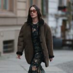 Diane Batoukina usa óculos escuros grandes quadrados marrom escuro da Dior, um pulôver de lã trançada rosa claro da Ralph Lauren, calça jeans azul desbotada / botões de cintura alta / pernas largas, uma bolsa branca latte de couro fosco 30 Montaigne da Dior, camurça branca e tênis de couro da Chanel, durante uma sessão de fotos de moda de estilo de rua, em 21 de abril de 2023 em Paris, França.