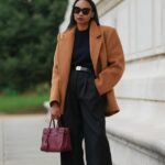 PARIS, FRANÇA - 31 DE DEZEMBRO: Yuwei Zhangzou usa cabelo preso em um rabo de cavalo trançado baixo, maquiagem com tez uniforme, sobrancelhas definidas e batom, fones de ouvido de arame, óculos de sol prateados ovais com lentes escuras da Celine, uma jaqueta de couro bomber marrom grande com gola alta e fecho de correr frontal, calça esportiva marrom de perna reta da Alo, uma pequena bolsa estruturada de shearling bege e marrom fofa com alça superior da Loro Piana, branca sapatos forrados de shearling com painéis de camurça marrom, cadarços contrastantes e sola plana de borracha da Moon Boot, segura um telefone celular, durante uma sessão de fotos de moda de rua, em 31 de dezembro de 2025 em Paris, França. (Foto de Edward Berthelot/Getty Images)