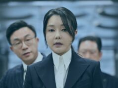 Ex-primeira-dama da Coreia do Sul condenada a 20 meses de prisão por corrupção Uma mulher de terno escuro e camisa branca olha diretamente para a câmera, com dois homens desfocados ao fundo.