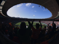 FIFA assina direitos exclusivos da Copa do Mundo de 2026 para a Stats Perform como distribuidora oficial global de direitos de apostas FIFA x Stats Perform. Torcedores comemorando dentro de um estádio de futebol lotado durante uma partida, vistos através de uma lente grande angular sob um teto oval aberto.