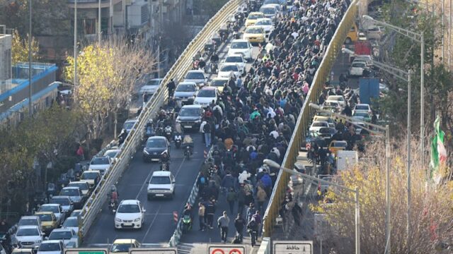 Uma foto de um vídeo supostamente mostra um manifestante sentado no meio de uma rua de Teerã, recusando-se a se mover, enquanto as forças de segurança avançam em motocicletas antes de espancá-lo. A imagem foi comparada ao “Homem Tanque” da Praça Tiananmen da China.