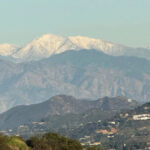 uma montanha coberta de neve é ​​vista pairando sobre as verdes montanhas de Santa Monica, em Los Angeles
