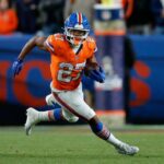 Um jogador do Denver Broncos com camisa laranja e capacete azul correndo com a bola de futebol.