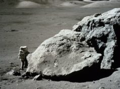 Já estivemos na lua, então por que vamos de novo? Quatro astronautas em trajes espaciais azuis estão na grama com um foguete laranja ao fundo.