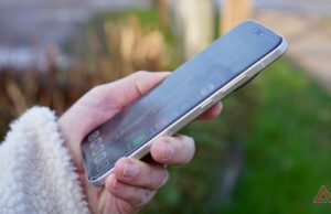 Já estou farto do meu telefone Android carro-chefe gago e lento Uma mulher sorridente está sentada com um smartphone na mão, ao lado de um grande telefone exibindo o ícone do aplicativo Reddit, enquanto o mascote do Android e o personagem Snoo do Reddit aparecem de forma divertida.