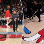 Três funcionários da arena limpam a quadra de basquete durante um jogo da NBA.