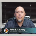 O presidente da tribo Lumbee, John L. Lowery, olhando para a câmera, sentou-se. Num ambiente de escritório, com as persianas fechadas atrás dele. Lumbee Tribe provoca possíveis planos de cassino após compra de terreno na Carolina do Norte