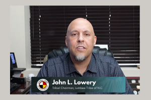 Lumbee Tribe provoca possíveis planos de cassino após compra de O presidente da tribo Lumbee, John L. Lowery, olhando para a câmera, sentou-se. Num ambiente de escritório, com as persianas fechadas atrás dele. Lumbee Tribe provoca possíveis planos de cassino após compra de terreno na Carolina do Norte