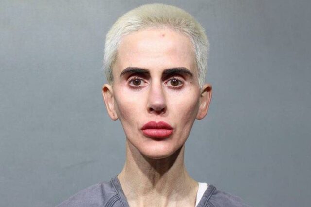 Foto de uma mulher com cabelo loiro curto e descolorido, sobrancelhas escuras proeminentes e batom vermelho, olhando diretamente para o espectador.