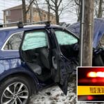 Um SUV azul após um acidente de carro, com airbags acionados e porta-malas aberto, e um bombeiro inspecionando a frente do carro fortemente danificada.