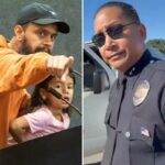 O vice-chefe do LAPD, Alan Hamilton, de uniforme e óculos escuros, olhando para a câmera, parado ao lado de uma van da polícia com a porta aberta.